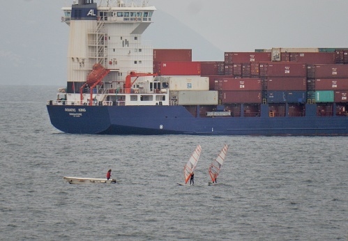 Naples, Campania, Italy - 10 March 2019: Windsurfers in the Gulf of Naples while transiting a container ship
