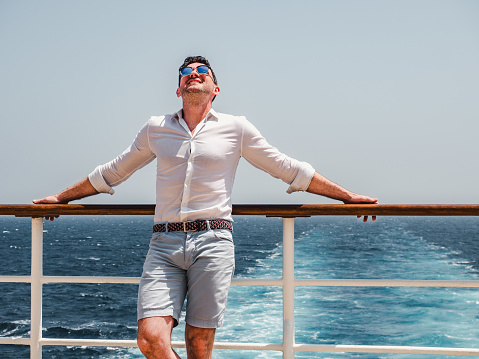 Fashionable man on the empty deck of a cruise liner against the backdrop of the sea waves. Side view, close-up. Concept of style, recreation and travel