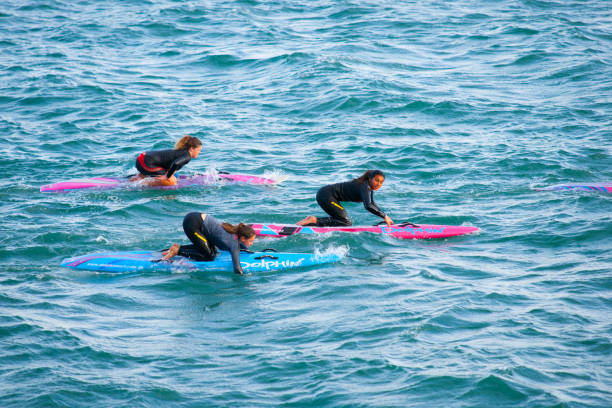 drei junge frau auf hellem paddelbrett auf türkisfarbenem meer. - editorial women paddleboard surfboard stock-fotos und bilder