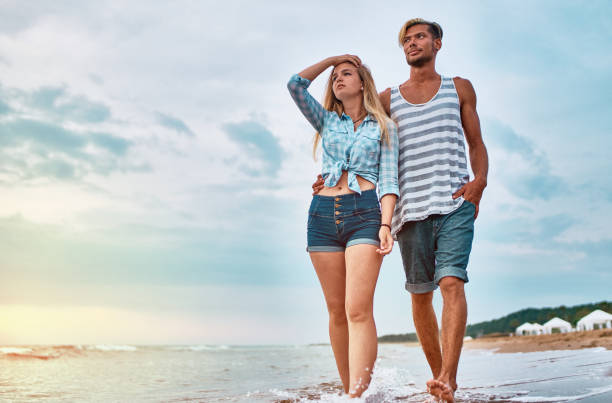 istock Young Couple walking along the beach at sunset 1140870928