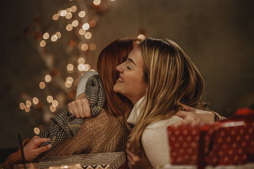 Young woman and her mother are hugging during opening Christmas presents.