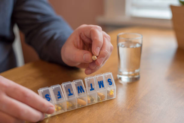 Man taking daily supplements from plastic pill organizer box stock photo