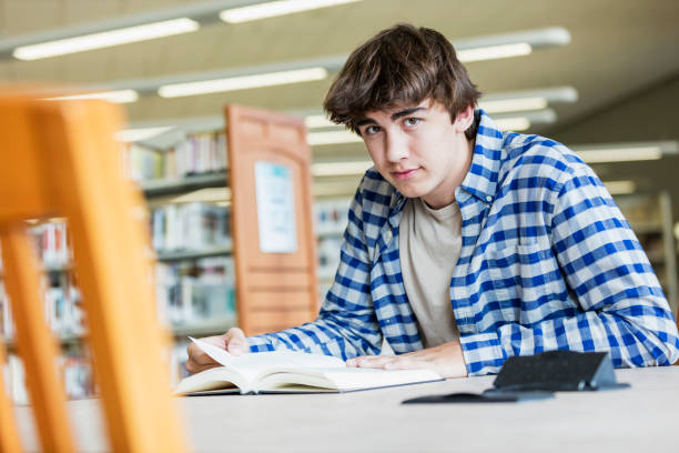 istock Teenage boy sitting at a table reading in the library 1140882518