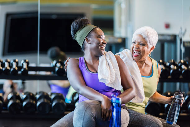 African-American women at the gym A senior African-American woman in her 60s exercising at the gym with her adult daughter, a young woman in her 20s. They are taking a break from lifting dumbbells, conversing and drinking from water bottles. health club stock pictures, royalty-free photos & images
