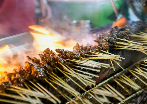 Roasting meat, chicken and mutton satays with charcoal, fire and smoke at night market in Singapore