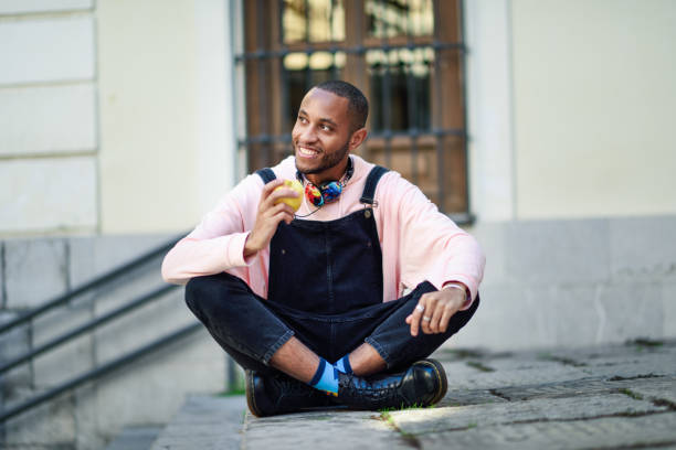 istock Young black man eating an apple sitting on urban steps. 1140901393