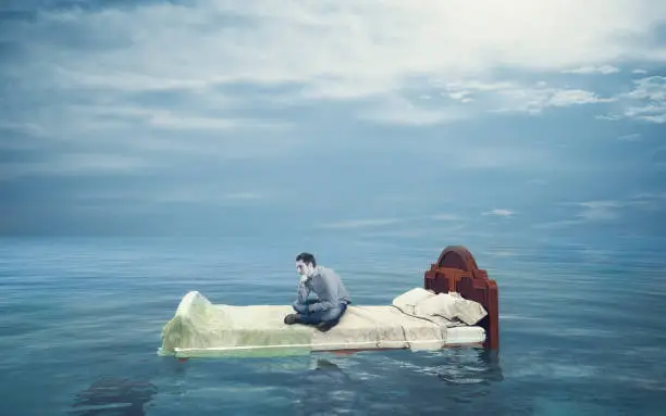 Confused man sitting on a bed in the ocean