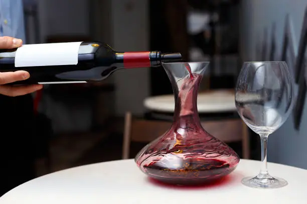 sommelier is pouring red wine into a decanter