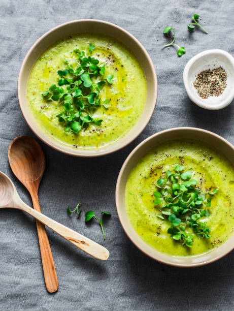 Mashed spring vegetable soup served with micro greens and whole grain crackers on a gray background, top view. Healthy vegetarian food concept