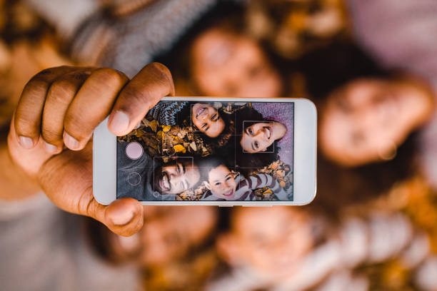 Close up of happy black family taking a selfie with cell phone in autumn leaves. Close up of happy African American family having fun while taking a selfie with mobile phone while relaxing in autumn leaves. camera phone photo stock pictures, royalty-free photos & images