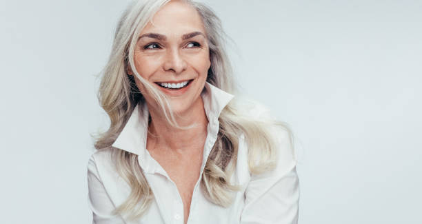 Mature woman with beautiful smile Elegant mid adult woman against white background. Stylish mature woman in white casuals looking away and smiling. grey hair stock pictures, royalty-free photos & images