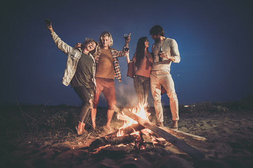 Two happy couples having fun by the campfire on the beach at night.