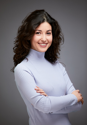 Close-up of an attractive middle aged woman with toothy smile wearing turtleneck sweater while standing at isolated grey background. Copy space. Studio shot.