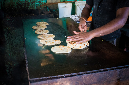 Traditional street food vendor. Man cooks and inverts indian flatbreads, roti or chapati, served with curry. Morning breakfast time. Paratha