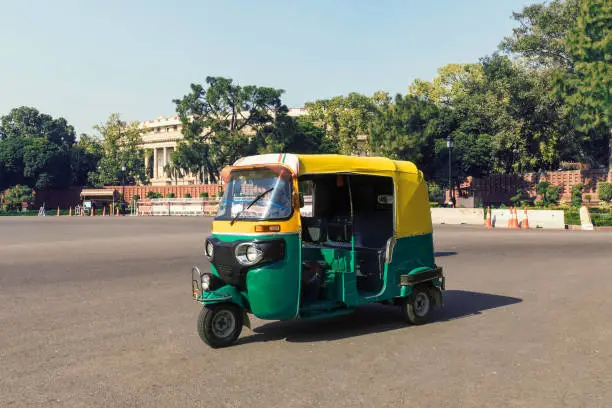 Tuk tuk - traditional indian moto rickshaw taxi on one of the street of New Delhi. yellow green tricycle stands on the square against the background of the presidential Palace. motorcycle 50-60 years