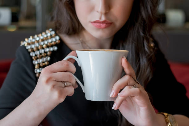 Girl in a black dress in a cafe drinking coffee from a white cup