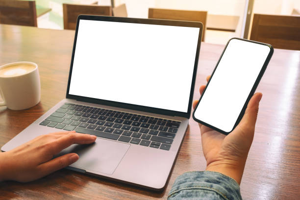 istock Mockup image of a woman touching on laptop touchpad with blank white desktop screen while using mobile phone 1140958262