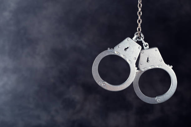 Handcuffs hanging on dark Handcuffs hanging against a dark background with copy space handcuffs stock pictures, royalty-free photos & images