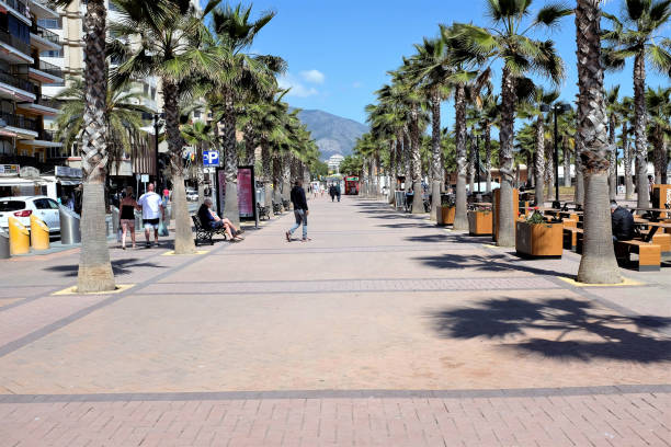 Fuengirola, Costa del Sol, Spain. March 28, 2019.  Holidaymakers enjoying the plaza Teresa Zabell a colonnade of palm trees on the promenade seafront at Fuengirola in Spain.