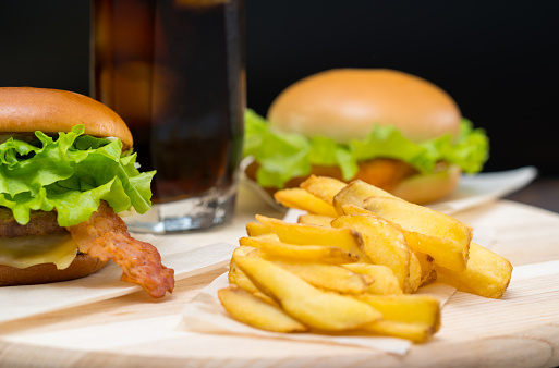 Portion of deep fried crispy potato chips served with a cheese ad bacon burger on a wooden board for a snack or lunch