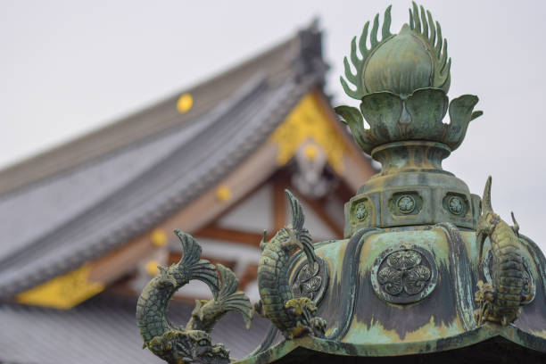 In the foreground a detailed japanese casting/sculpture decorated with fish, in the background a Japanese temple with golden highlights