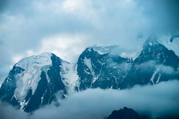istock Low cloud before huge glacier. Giant snowy rocky mountains under cloudy sky. Thick fog in mountains at early morning. Impenetrable fog. Cold rocks. Dark atmospheric landscape. Tranquil atmosphere. 1140973556