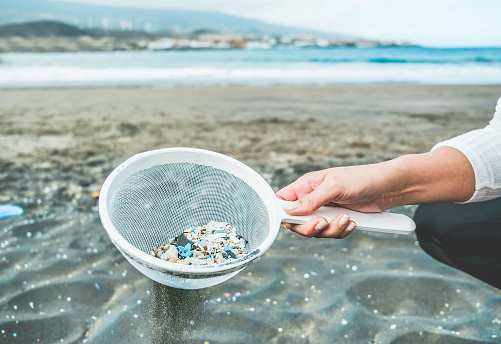 Mujer joven limpiando microplásticos de arena en la playa-problema medioambiental, contaminación y concepto de advertencia del sistema ecológico-enfoque a mano photo