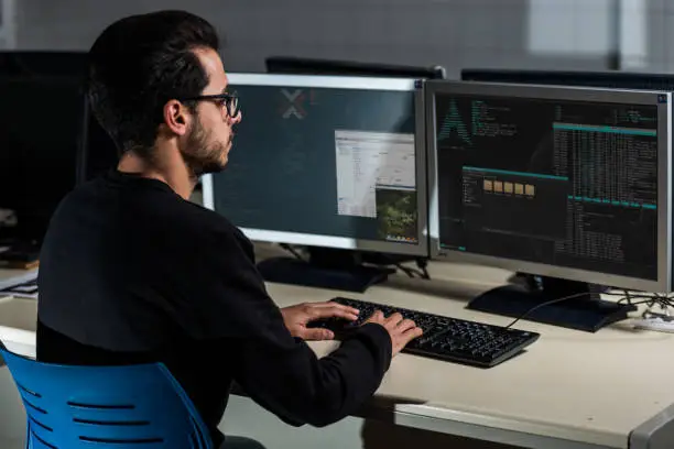 Photo of Young computer science student developing with his computer on a Linux System over double screen system