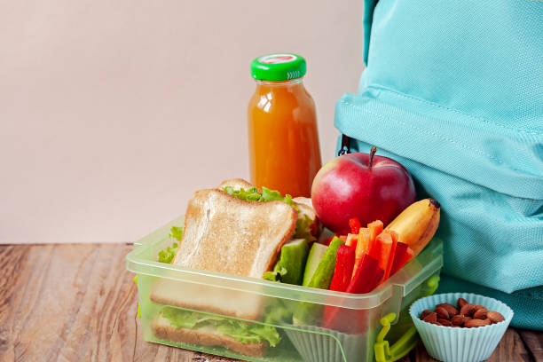 istock Lunch box with appetizing food and backpack on wooden table. 1140987898