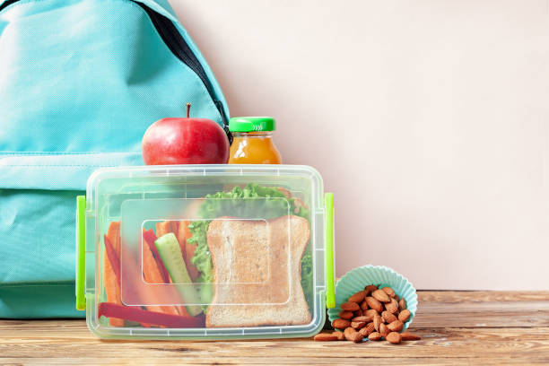 School lunch box with sandwich, vegetables, juice and almonds on table. stock photo