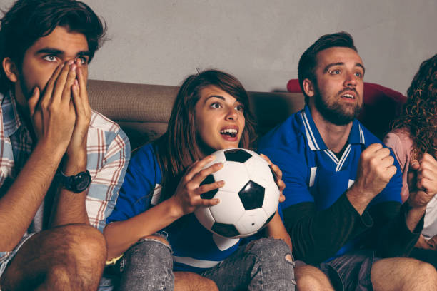 Friends watching football Group of young friends watching a football match on a building rooftop, cheering and yelling, excited about the game excited football fan cheering for his team on tv stock pictures, royalty-free photos & images