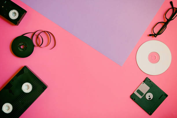istock Retro storage devices: plate, two videocassette, floppy disk, CD and glasses. Outdated technology concept on pink and violet paper background, top view, minimalism 1140988239