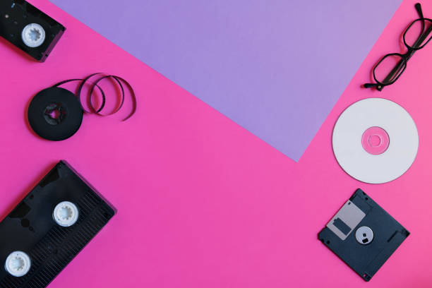 istock Retro storage devices: plate, two videocassette, floppy disk, CD and glasses. Outdated technology concept on pink and violet paper background, top view, minimalism 1140988241