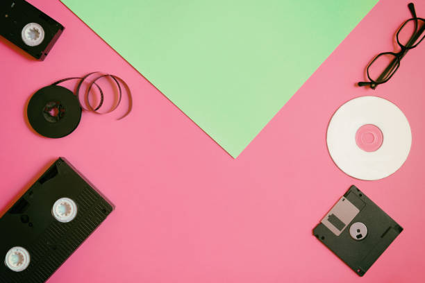 istock Retro storage devices: plate, two videocassette, floppy disk, CD and glasses. Outdated technology concept on pink and mint paper background, top view, minimalism 1140988257