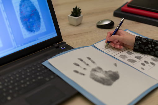 The forensic expert studies the fingerprints taken of a suspect. Detective expert writes data into the fingerprint table