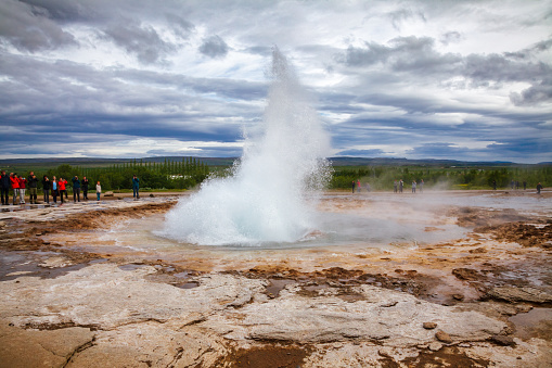 Haukadalsvegur, Iceland - July 21, 2015: Tourists observing eruption of the Strokkur geysir at Haukadalur geothermal valley. Strokkur (icelandic for churn) is one of most famous geysers in Iceland erupting every 6\