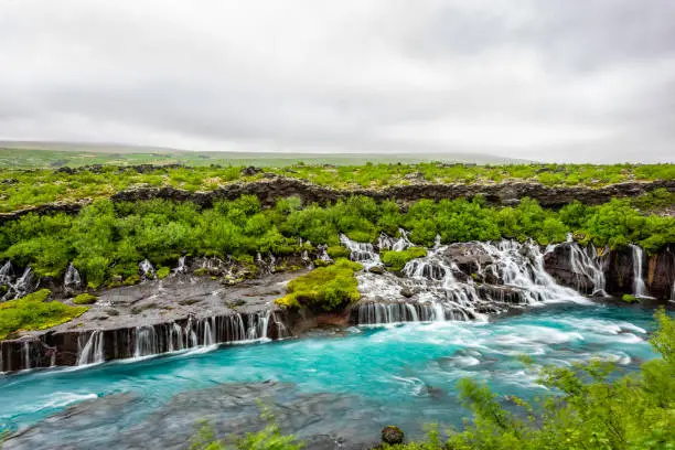 Photo of Colorful blue aqua turquoise vibrant color water waterfall azure cascades Hraunfossar Lava Falls in Iceland with rainy cloudy landscape view