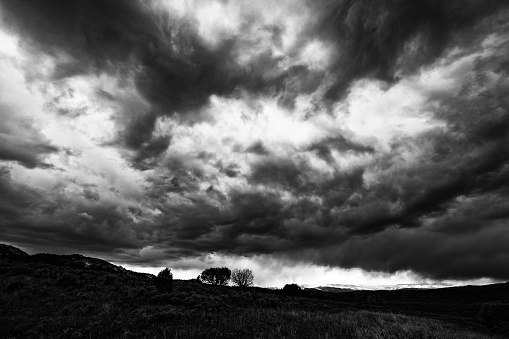 Dramatic Storm Clouds Landscape at Sunset - Clouds rolling in during storm right at sunset with mountain views. Black and white high-contrast dramatic photo.