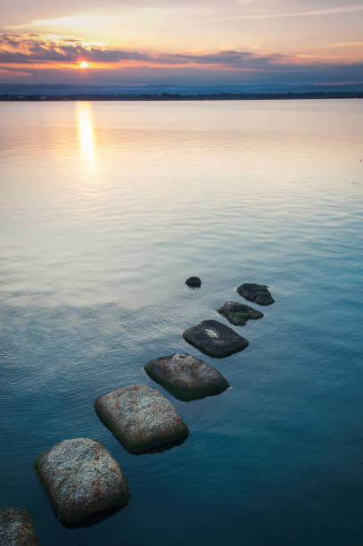 istock Spectacular sunset on water with stones on colorful cloudscape background 1140999891