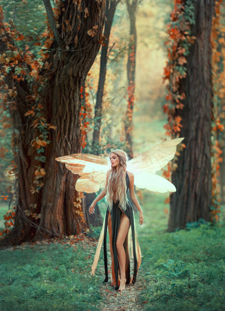 Incredible Fairy Walks In The Autumn Forest A Blonde Girl With Very Long  Hair Unusual Styling Elf In A Green Dress With Glowing Golden Wings  Background Of Huge Old Trees Entwined With