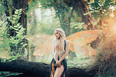 real fairy from magical stories, goddess of nature with transparent wings alone in dense forest, beauty closes her eyes, listens to birds singing, charming lady in the sunlight and with bare legs