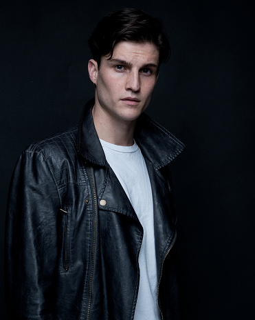 Close up view of attractive man wearing leather jacket and is on black background