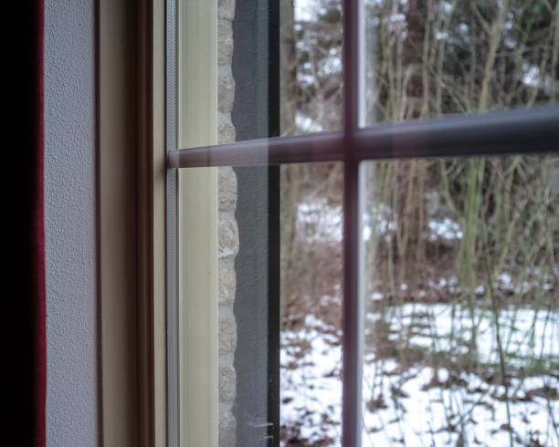 istock Window frame with a transparent double glazing and decorative elements inside the glass, in a brick house, against the background of a snow-covered yard and trees. 1141009578