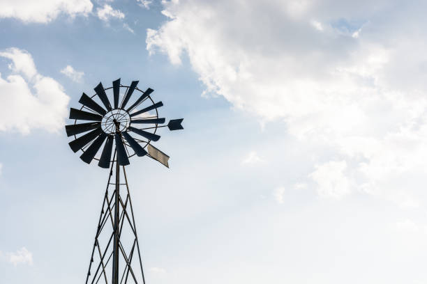 istock Old-fashioned metal wind powered water pump against pale blue sky with white clouds. 1141009844