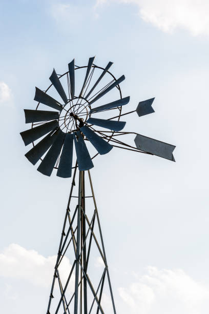 istock Old-fashioned metal wind powered water pump against pale blue sky with white clouds. 1141009846