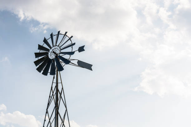 istock Old-fashioned metal wind powered water pump against pale blue sky with white clouds. 1141009847