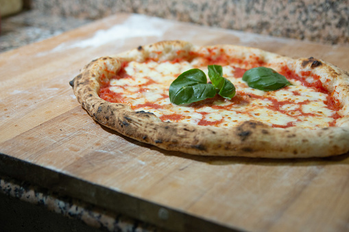 Pizza Margherita cooked with basil, on a wooden cutting board, with flour at the base