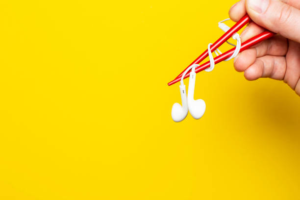 istock Hand  is holding a headphones using chopsticks on a bright yellow background, with copy space. Concept of musical taste. 1141011140