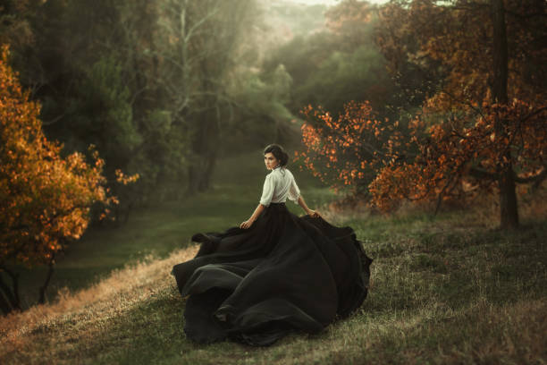 mysterious girl with dark hair and a long flying black vintage dress runs through the woods, a charming ambush, a great attractive witch turns into a crow, waving a train like bird wings A girl in a vintage dress is running and looking around. The train waving in the wind. Artistic Photography blouse photos stock pictures, royalty-free photos & images