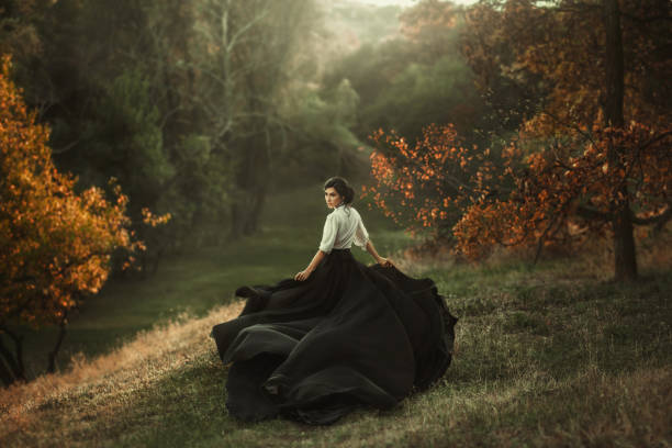 mysterious girl with dark hair and a long flying black vintage dress runs through the woods, a charming ambush, a great attractive witch turns into a crow, waving a train like bird wings A girl in a vintage dress is running and looking around. The train waving in the wind. Artistic Photography white shirt black skirt stock pictures, royalty-free photos & images
